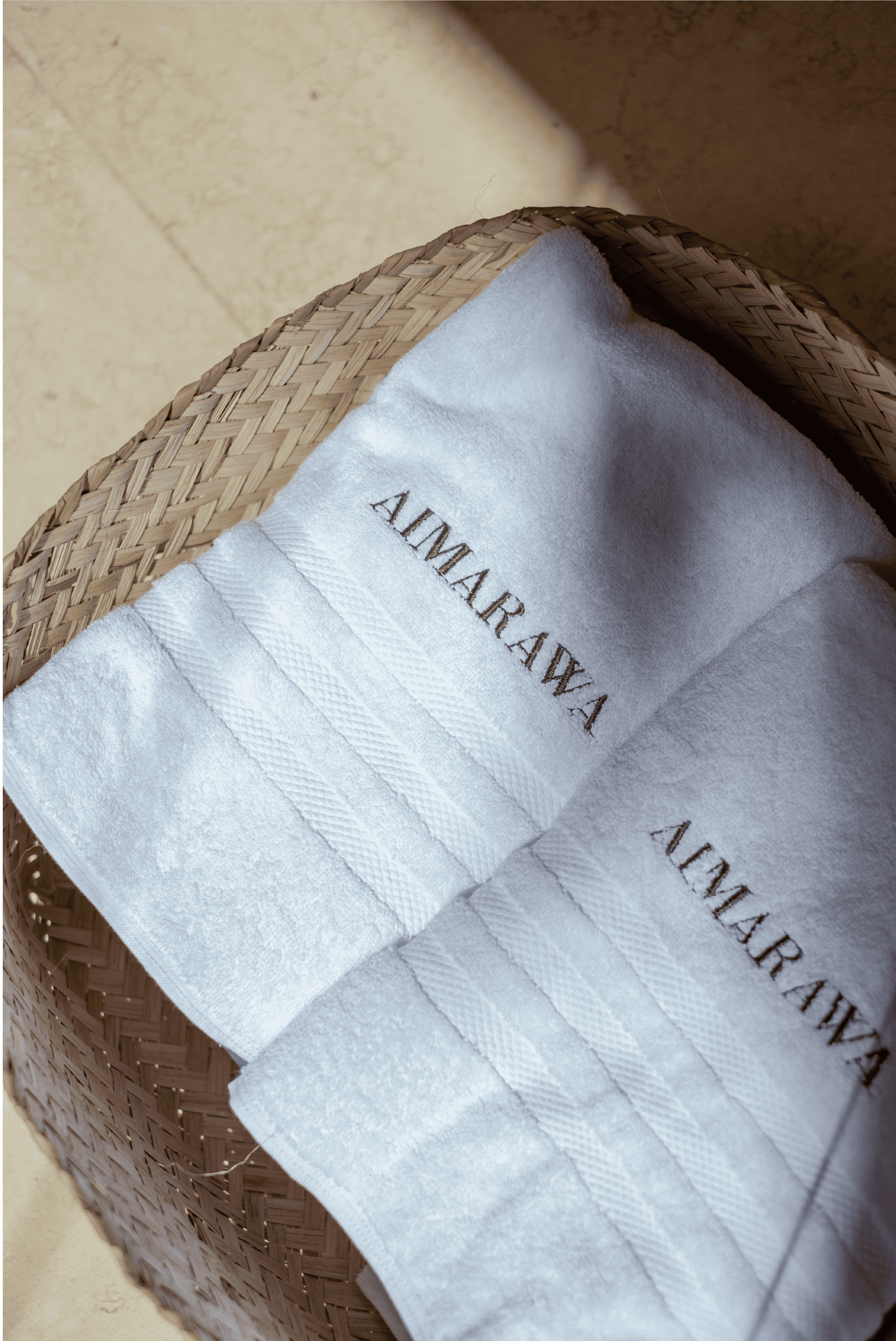 Elegant white luxury towels with "AIMARAW" branding in a woven basket.