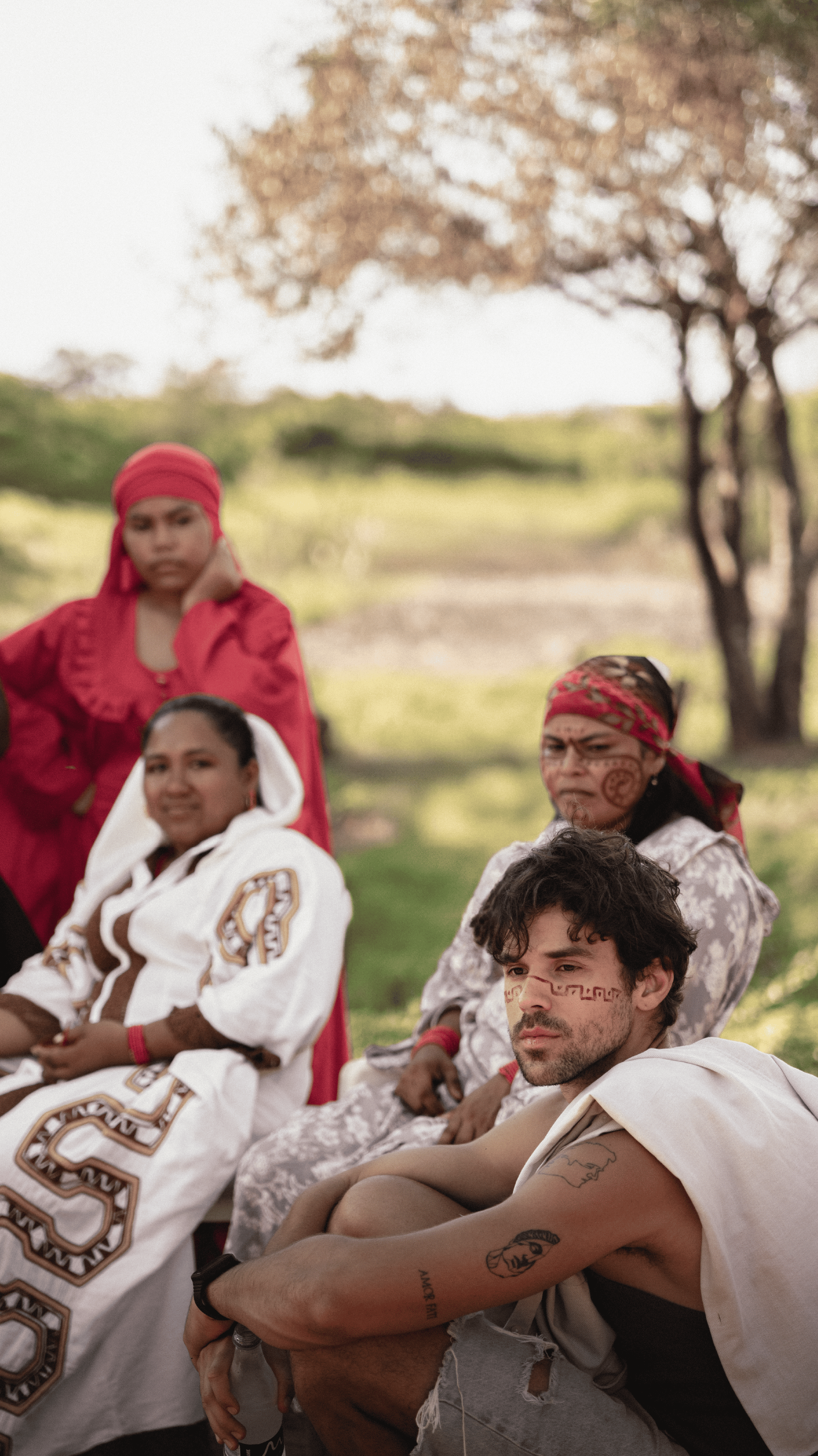 An image of a group of indigenous women and a man sitting outdoors in a natural setting, showcasing.