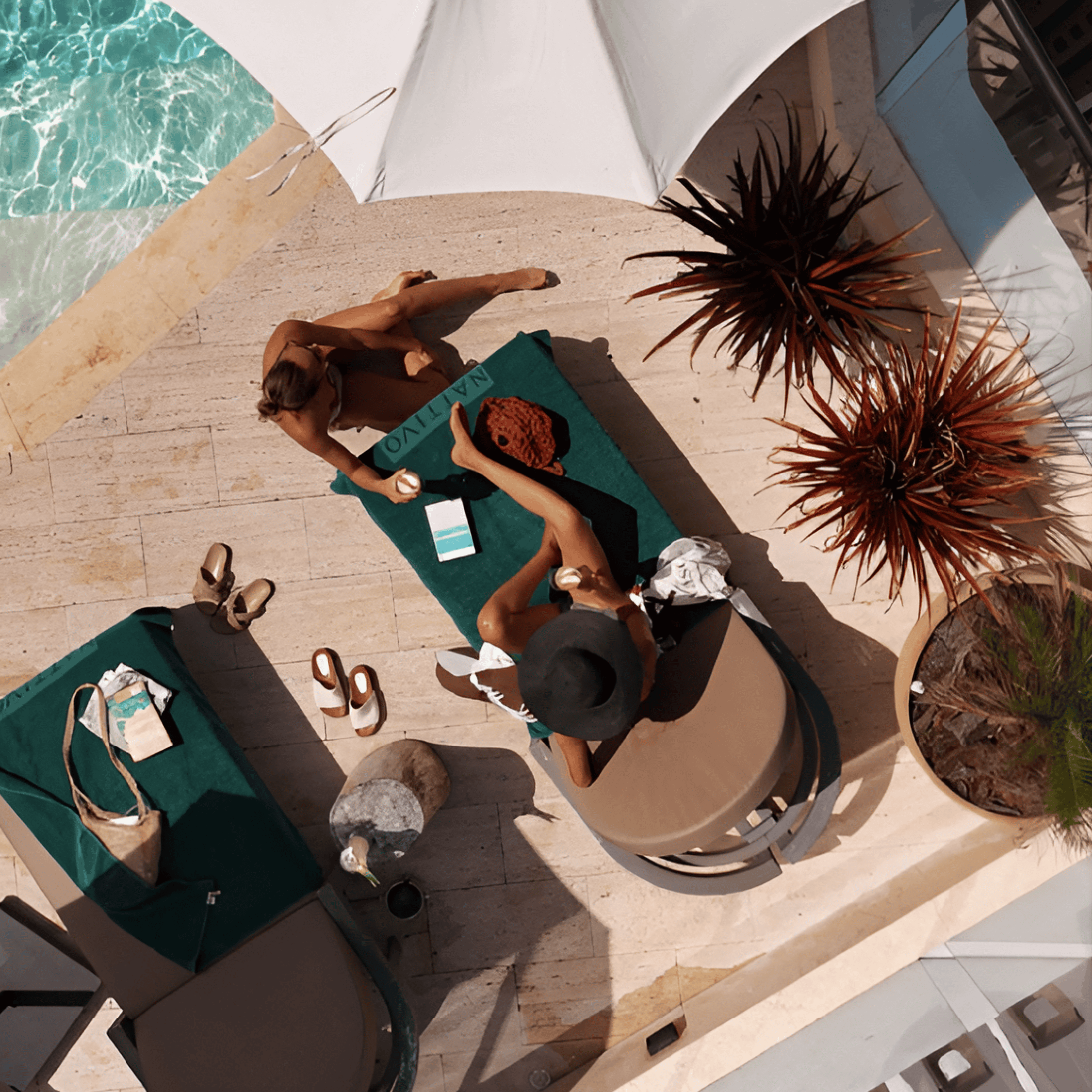Relaxing poolside scene with women enjoying sunbathing and drinks under umbrellas.