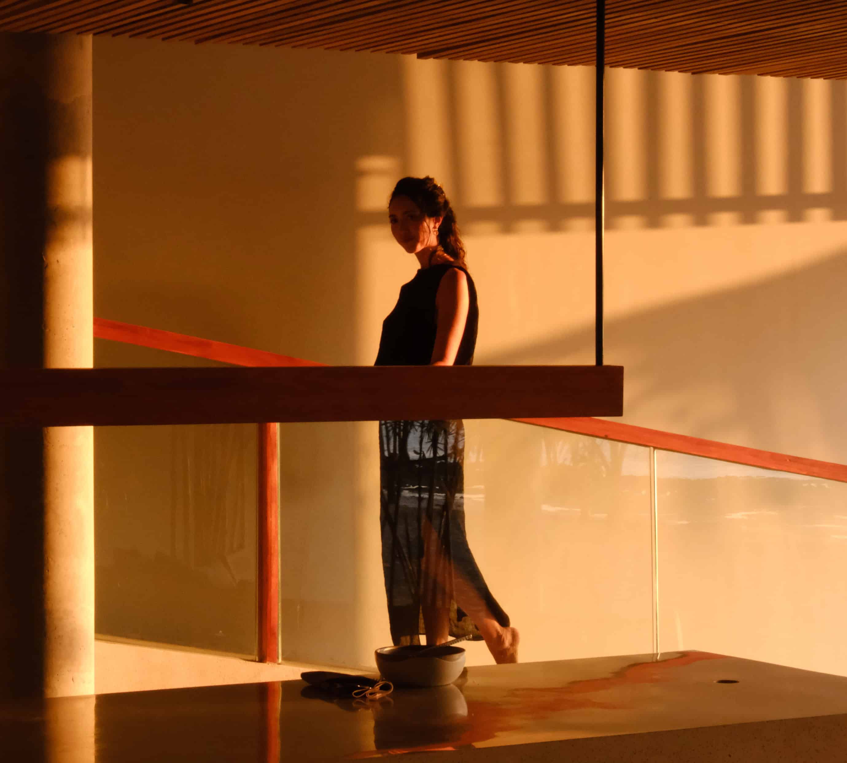 Stylish woman standing on a balcony during sunset with modern architecture and warm lighting.