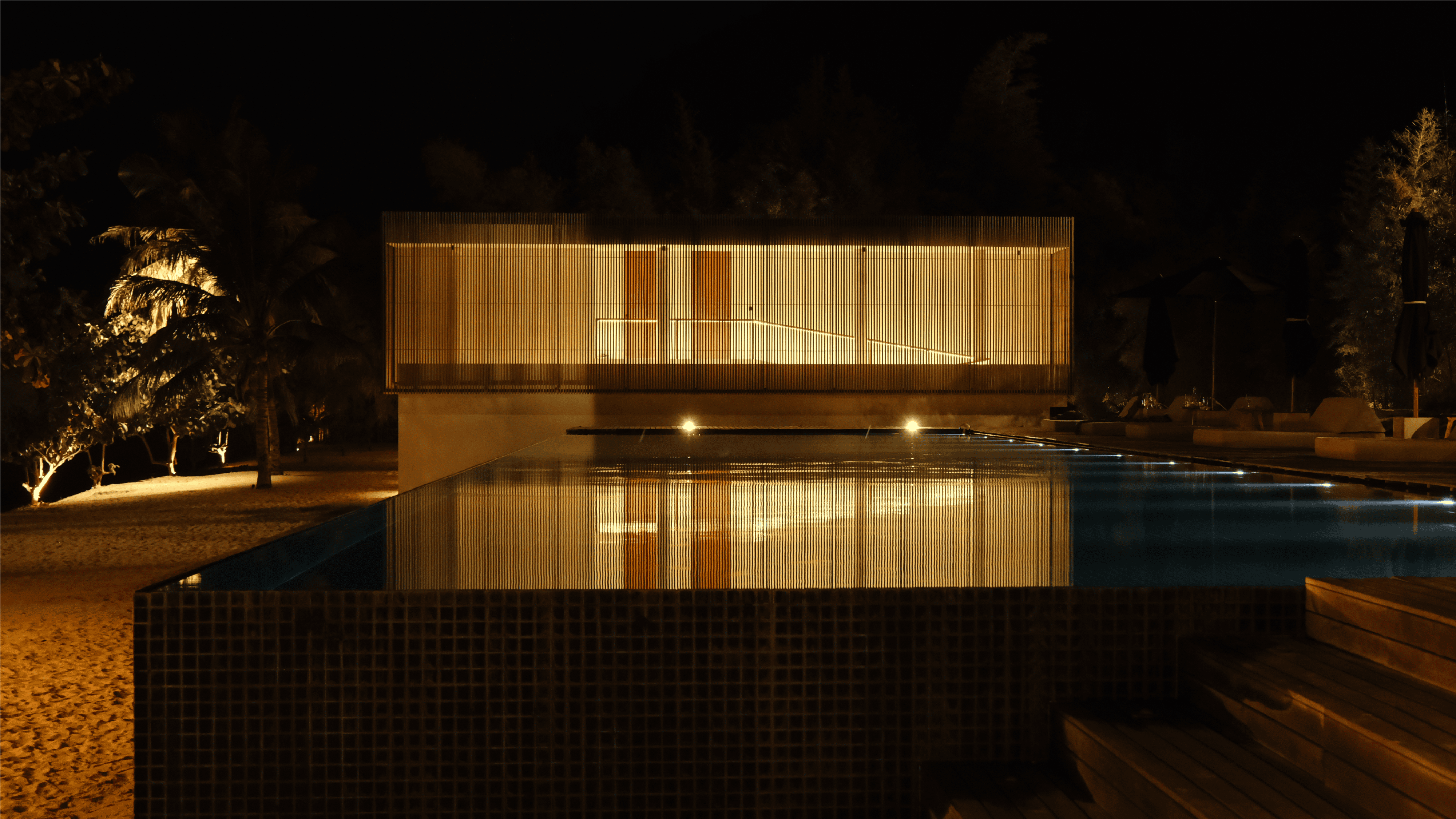 Luxury outdoor pool with ambient lighting and lush greenery at night.