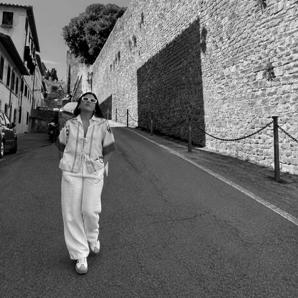 Stylish woman walking on a historic street with stone walls and buildings.