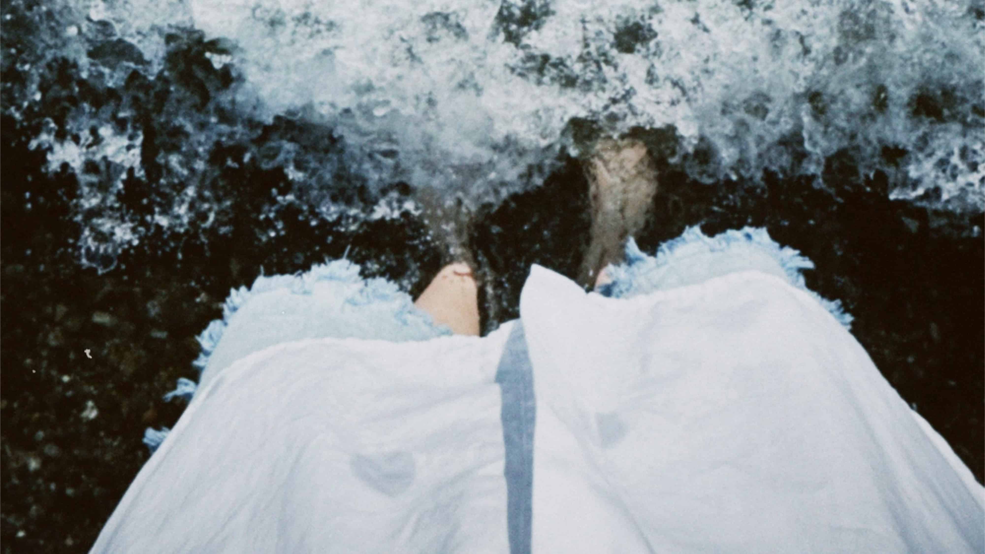 Woman in white dress standing near water with waves crashing.