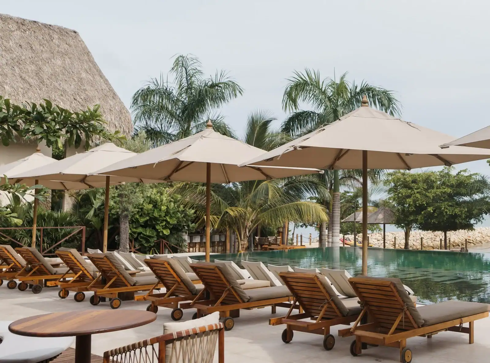 Relaxing poolside lounge with wooden sunbeds and umbrellas in a tropical resort setting.