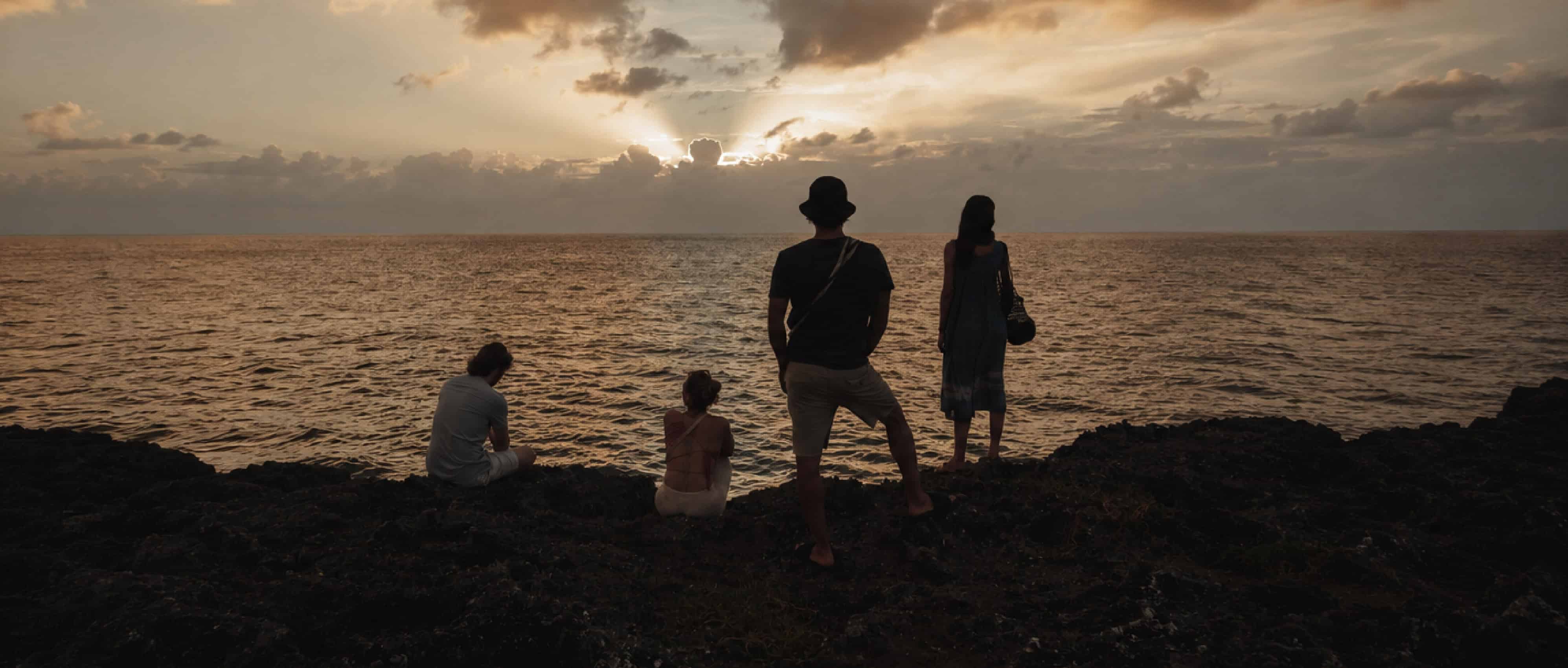 Sunset over the ocean with four people enjoying the scenic view from rocky shoreline.