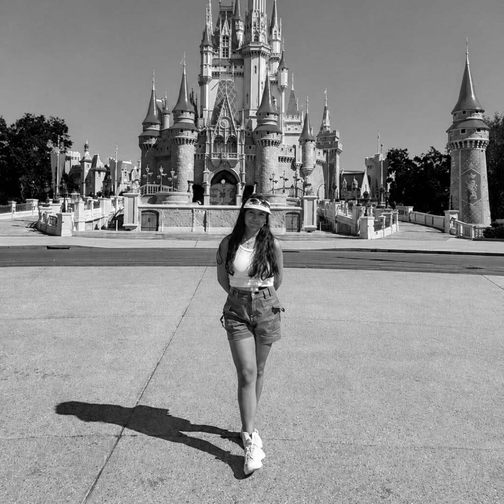 Young woman standing in front of Disney castle in black and white photo.