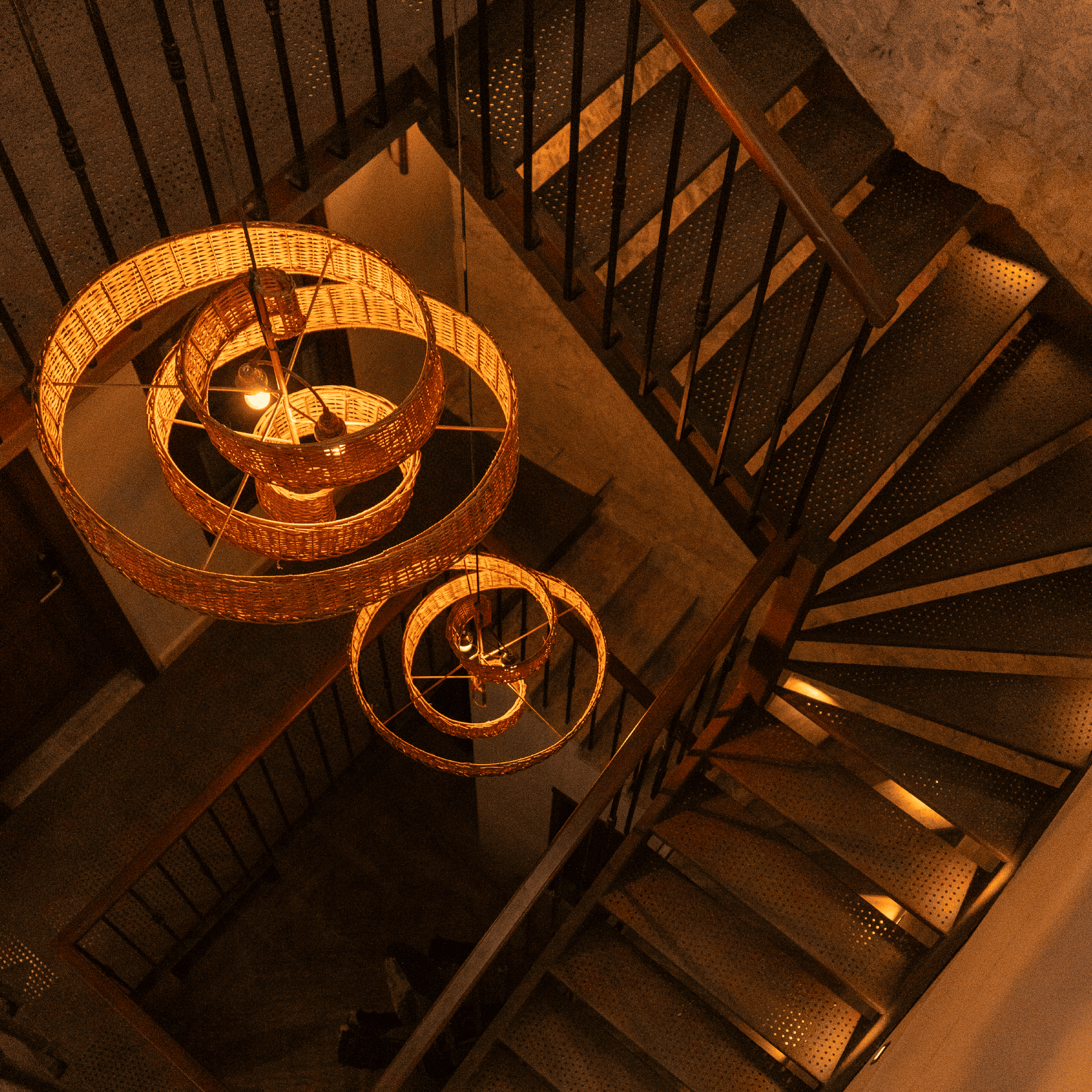 Elegant spiral staircase illuminated by wicker pendant lights in a stylish interior setting.