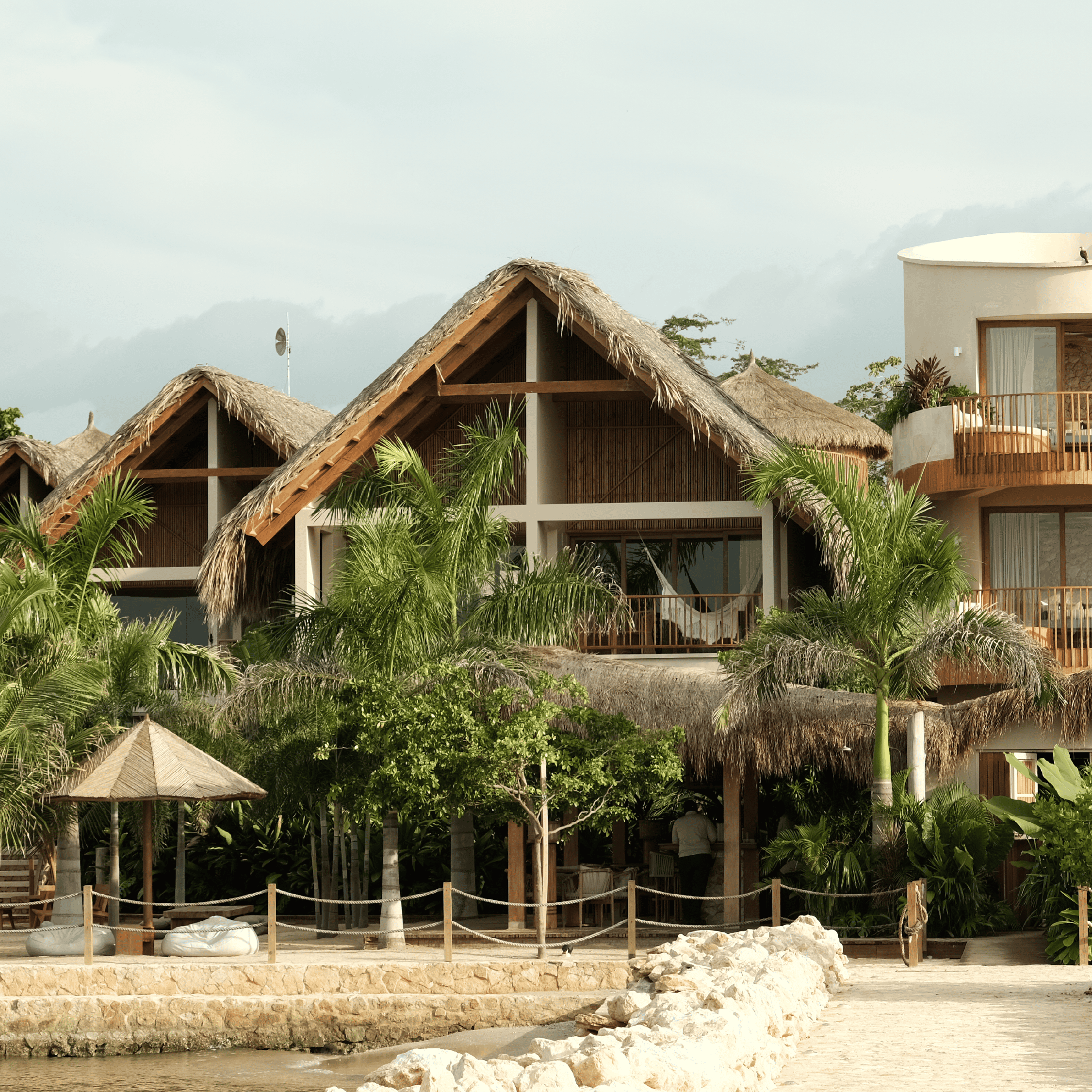 Beachfront tropical resort with thatched-roof bungalows, palm trees, and lush greenery.