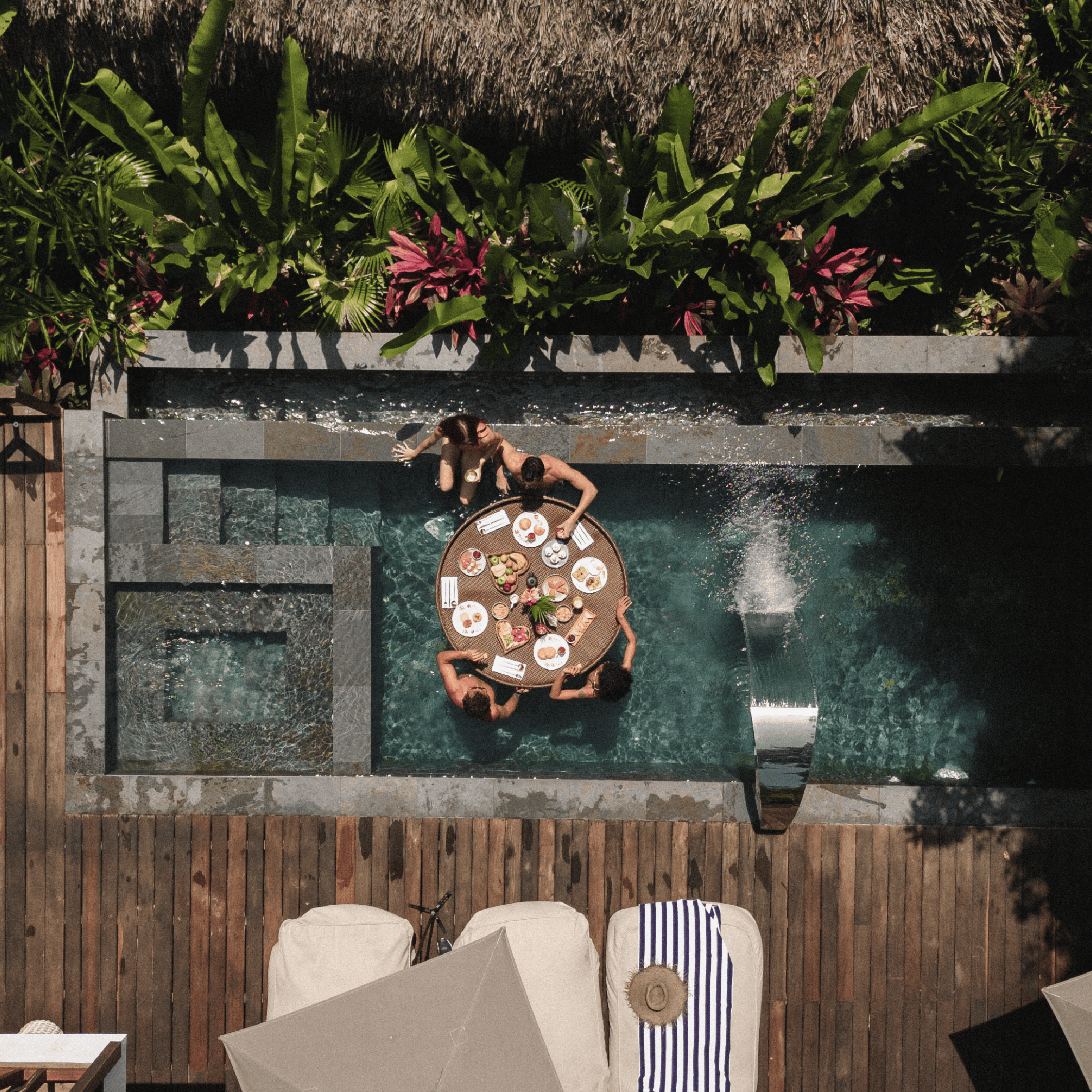 Elegant outdoor pool area with a dining table, tropical greenery, and relaxing lounge chairs.