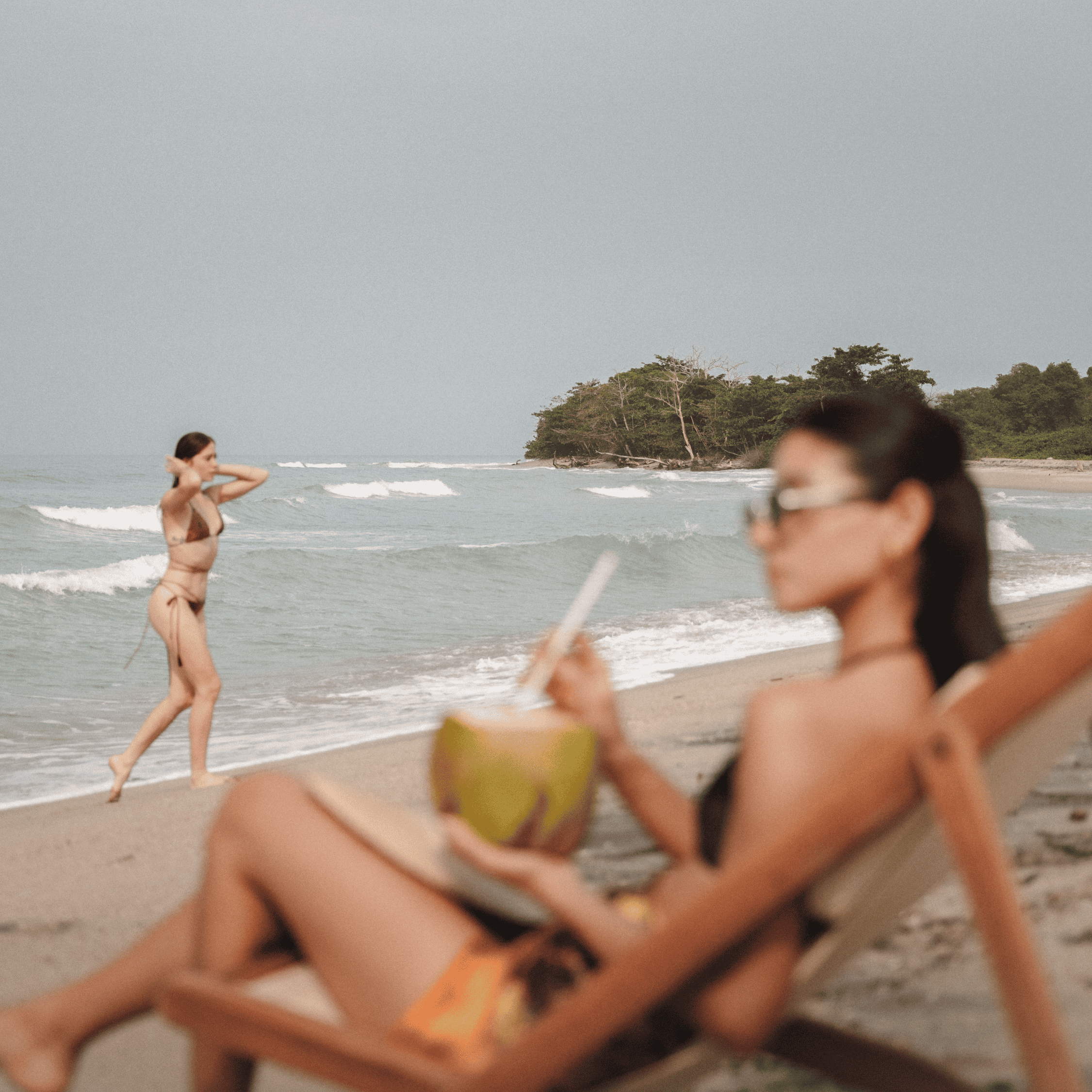Relaxing beach scene with women enjoying the seaside, one lounging with a coconut drink and the othe.