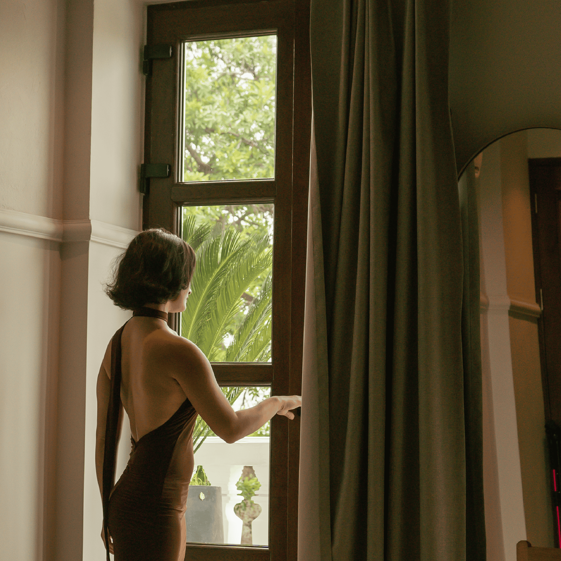 Woman gazing out of window in a modern, stylish interior with lush greenery outside.