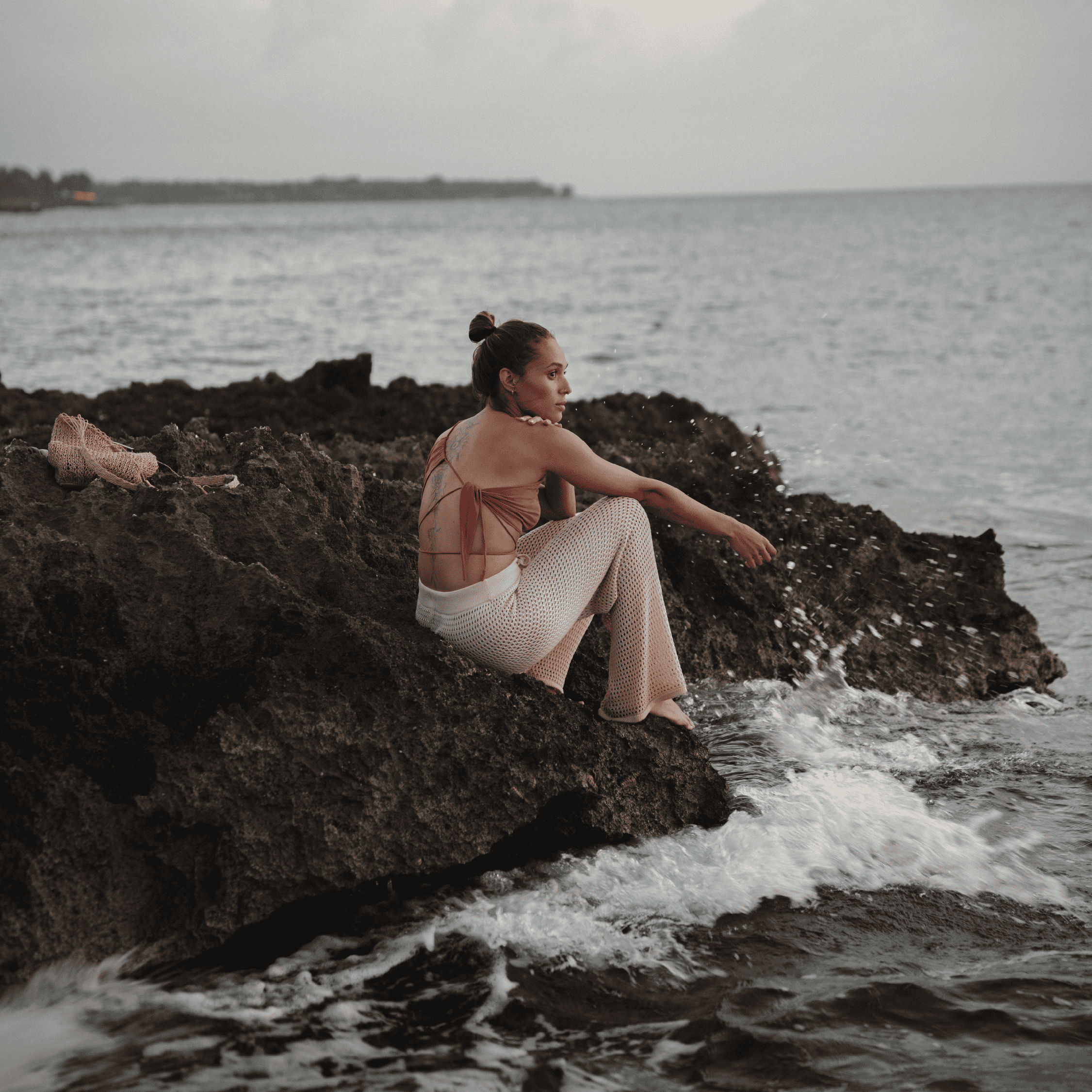 Woman relaxing on rocky shoreline with ocean waves in the background.
