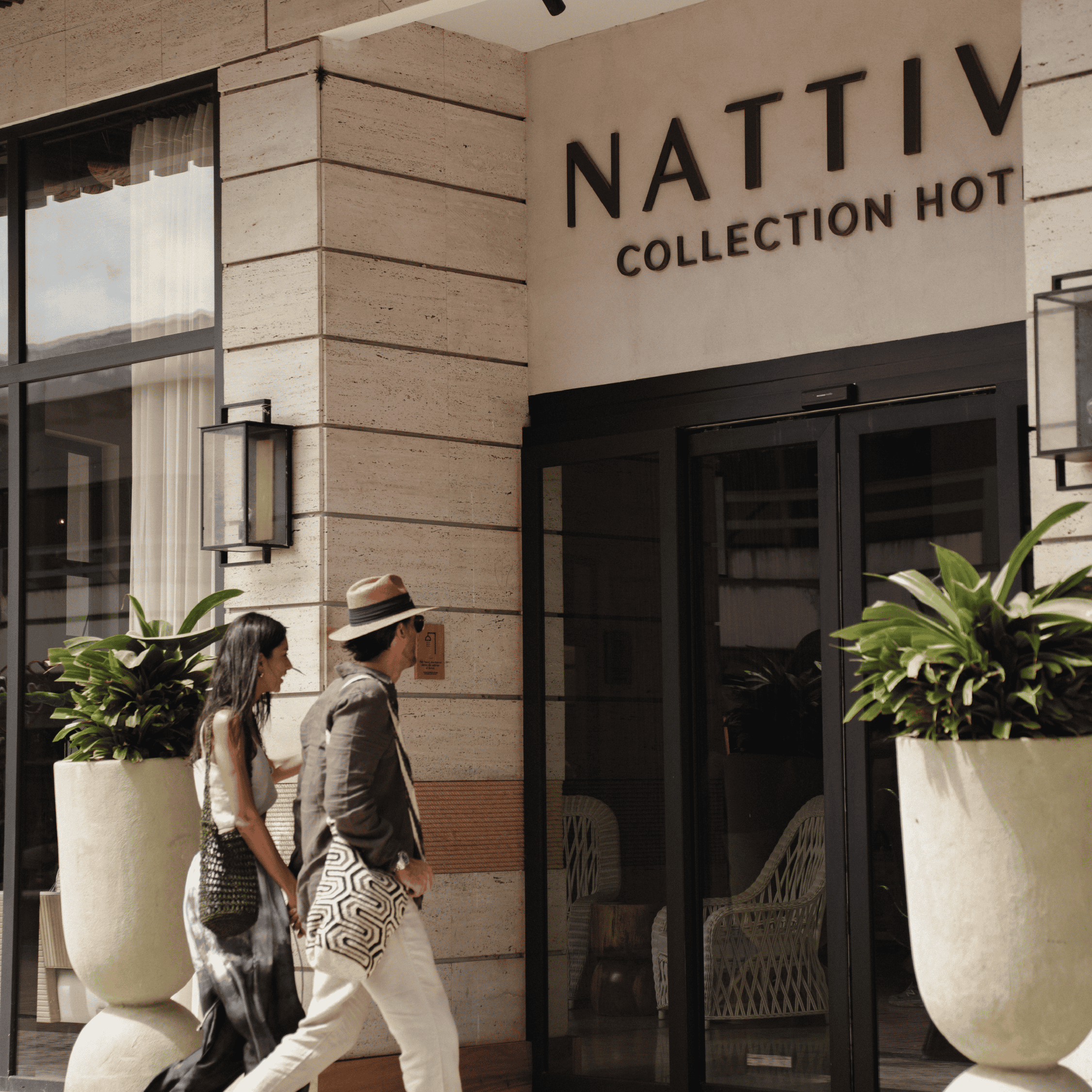 Guests entering Nattiv Collection Hotel with large potted plants outside.