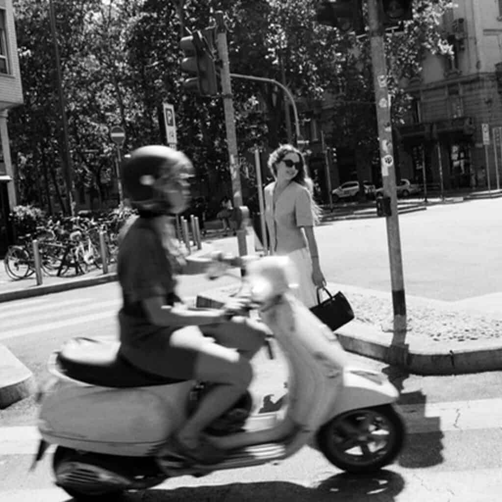 Scooter rider and woman crossing street at urban intersection in black and white.