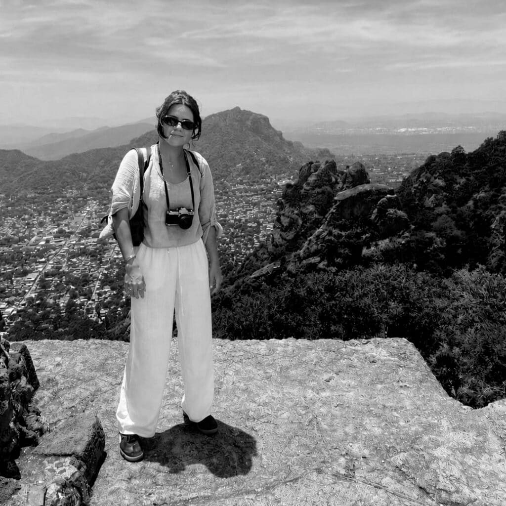 Woman with sunglasses and camera enjoying mountain view in black and white.