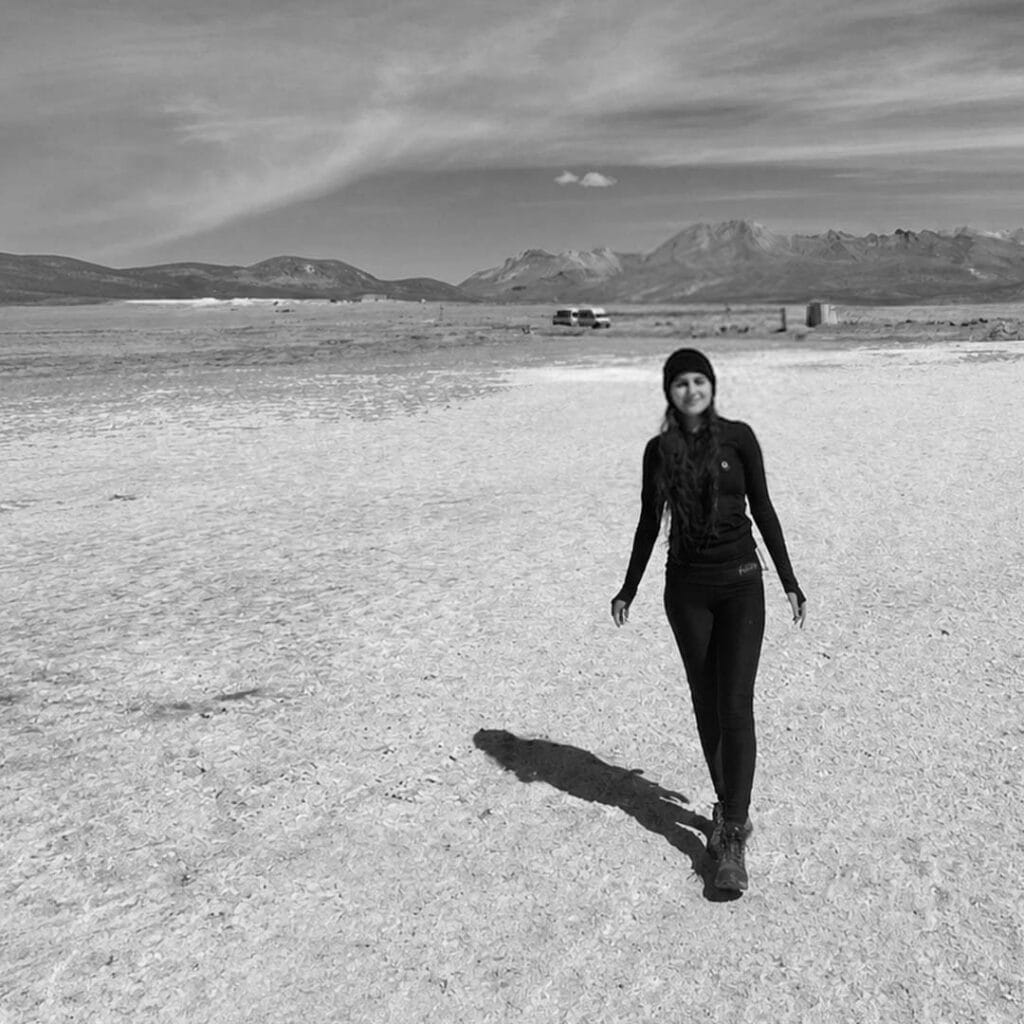 Woman walking in a vast desert landscape with mountains in the background.