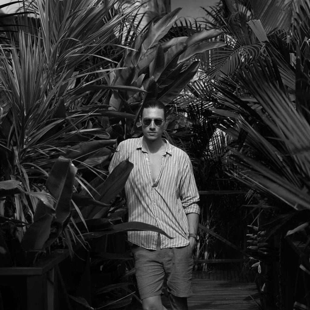 Man wearing sunglasses and striped shirt in lush tropical jungle.